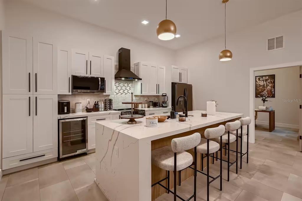 A modern kitchen features white cabinetry, a marble-topped island with bar seating, and pendant lighting — 13509 PARK BOULEVARD, SEMINOLE, FL