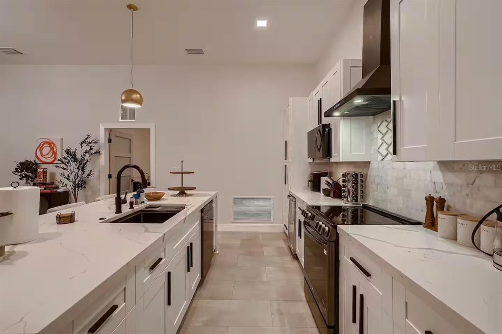 A modern kitchen features white cabinets, marble-look countertops, a large island, and dark appliances — 13509 PARK BOULEVARD, SEMINOLE, FL