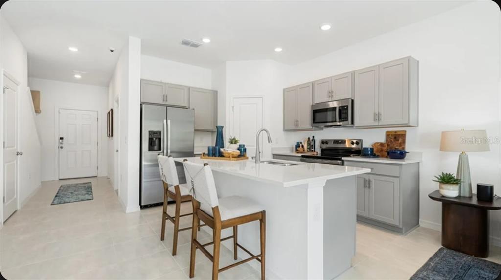 A kitchen with gray cabinets and a white island features bar stools and an adjacent living area — 7199 GRAND FOREST WAY, NOKOMIS, FL