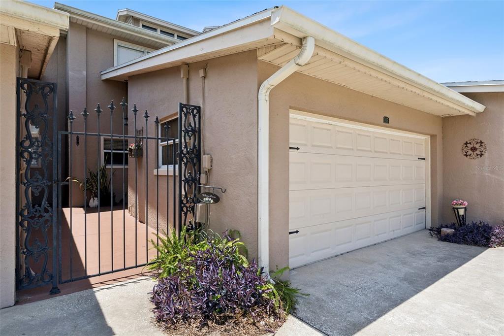 A beige house exterior features a white garage door, a wrought iron gate, and landscaping — 815 CHESTNUT STREET, CLERMONT, FL