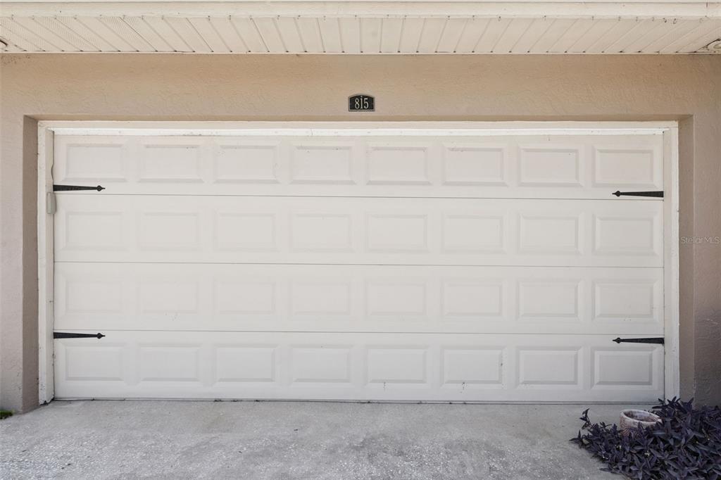 A white, paneled garage door with decorative black hinges is centered on a beige wall — 815 CHESTNUT STREET, CLERMONT, FL