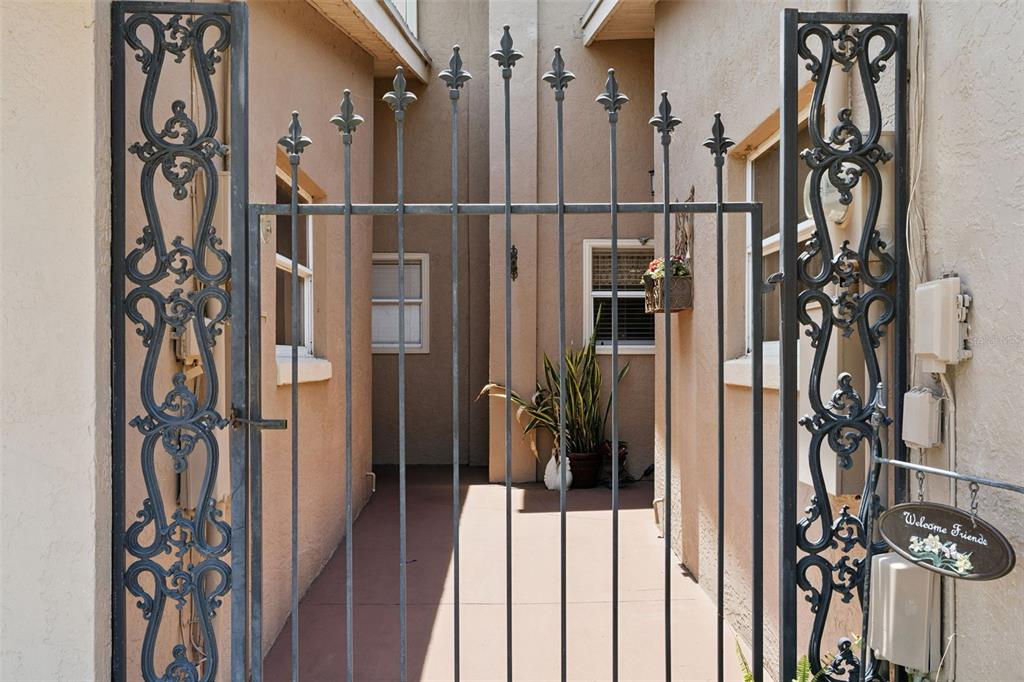 A black wrought iron gate opens to a narrow walkway between two beige stucco walls — 815 CHESTNUT STREET, CLERMONT, FL