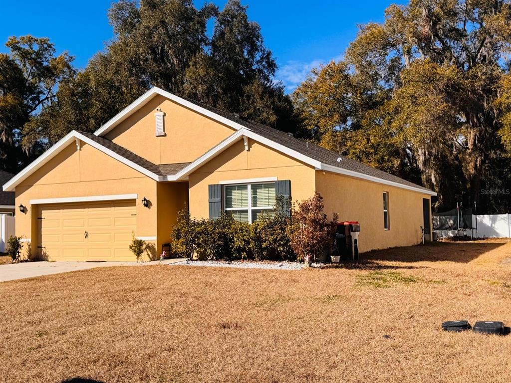 A single-story tan stucco house with a two-car garage and dark shutters — 3783 SE 97TH LANE, BELLEVIEW, FL