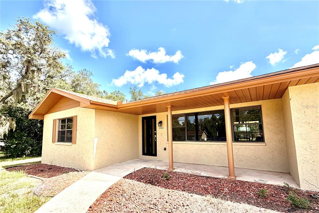 A single-story house with a tan stucco exterior, a covered porch, and a brown roof — 2404 N COCHRANE ROAD, AVON PARK, FL