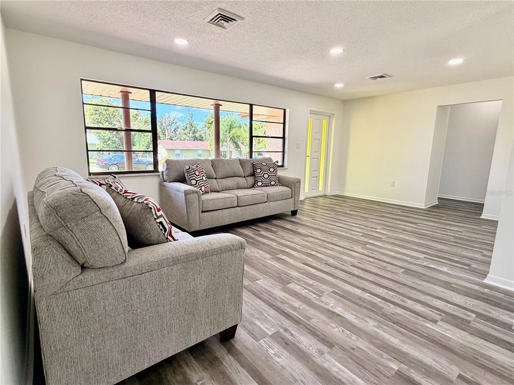 A living room features gray wood-look flooring, two gray sofas, and a large window — 2404 N COCHRANE ROAD, AVON PARK, FL
