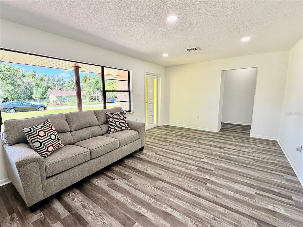 A living room features gray wood-look flooring, a gray sofa, and a large front window — 2404 N COCHRANE ROAD, AVON PARK, FL