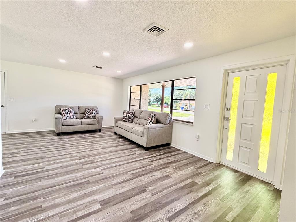 A living room features gray wood-look flooring, two gray sofas, and a white front door — 2404 N COCHRANE ROAD, AVON PARK, FL