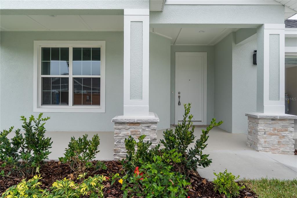 A front porch with stone-based columns, a white door, and a window with muntins — 4545 FAIRWAY OAKS DRIVE, MULBERRY, FL