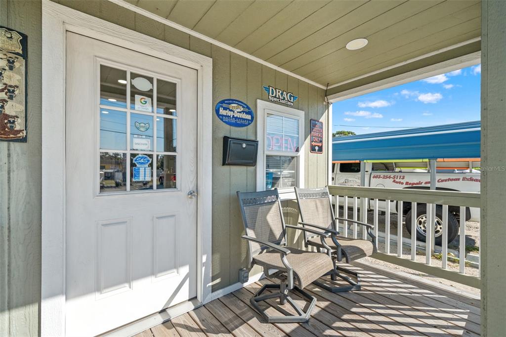 A covered front porch features two outdoor chairs, a white door, and a wooden deck — 9539 STATE ROAD 52, HUDSON, FL