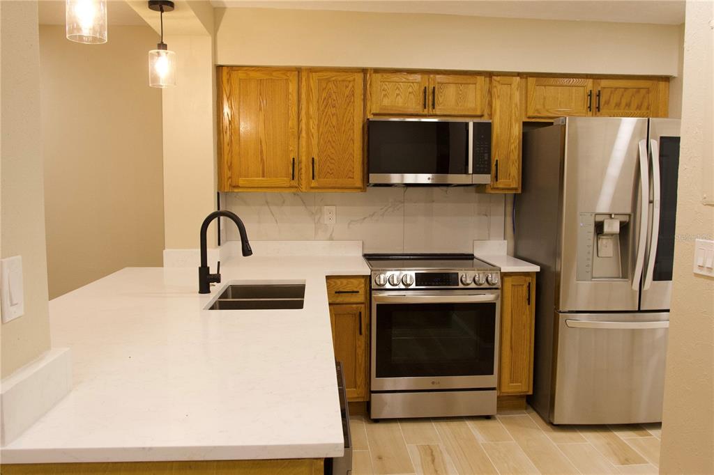 A kitchen features wood cabinets, stainless steel appliances, and a white quartz countertop island — 5313 INDIAN CREEK DRIVE UNIT D04, ORLANDO, FL