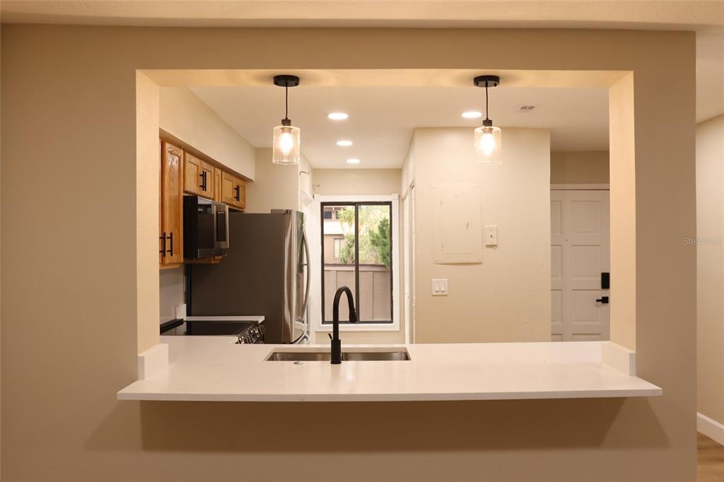 A kitchen view through a pass-through window features white countertops, a sink, and pendant lighting — 5313 INDIAN CREEK DRIVE UNIT D04, ORLANDO, FL