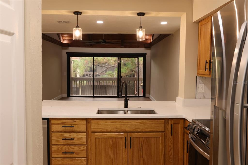 A kitchen with wood cabinets and a white countertop overlooks a room with sliding doors — 5313 INDIAN CREEK DRIVE UNIT D04, ORLANDO, FL