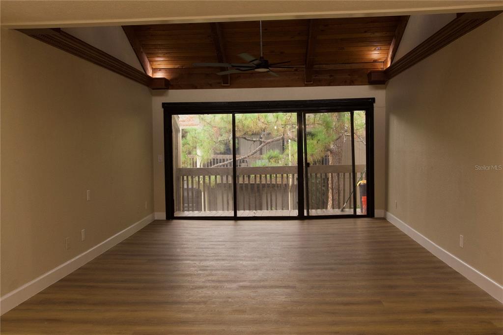 An empty room features wood-look flooring, a vaulted wood-plank ceiling, and sliding glass doors — 5313 INDIAN CREEK DRIVE UNIT D04, ORLANDO, FL
