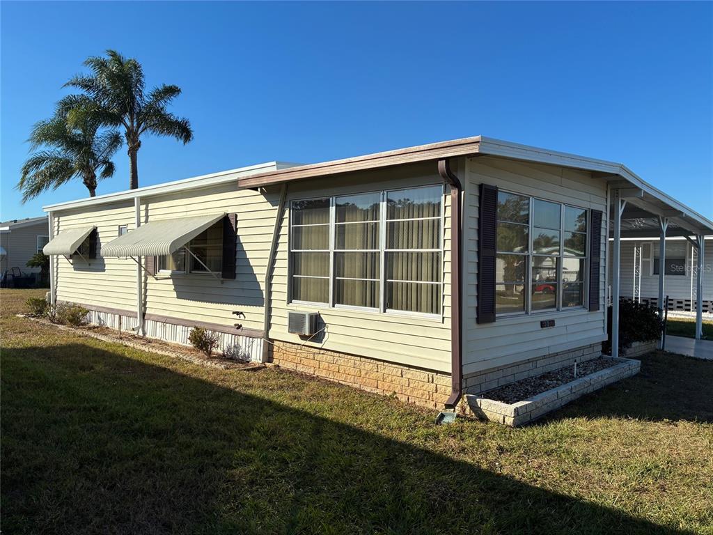 A side view of a light-colored mobile home with metal awnings and a brick-patterned base — 3211 LANARK DRIVE, HOLIDAY, FL