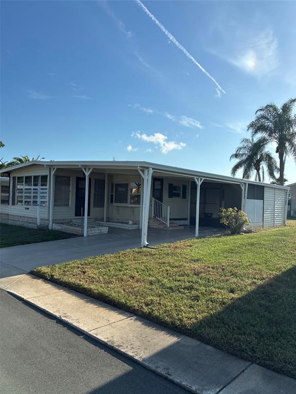 The exterior of a light-colored manufactured home features two window awnings and an air conditioning unit — 3211 LANARK DRIVE, HOLIDAY, FL