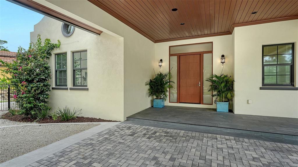 A paved driveway leads to a covered entryway with a wooden door and two potted plants — 360 N POINT ROAD, OSPREY, FL