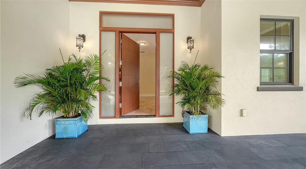 An open front door leads into a home entrance with two potted plants on a patio — 360 N POINT ROAD, OSPREY, FL