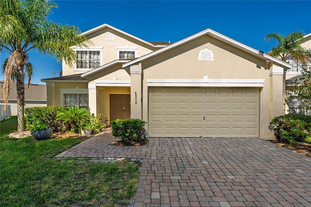A two-story suburban house features a tan stucco exterior, a paved driveway, and a garage — 1202 CUMBRIAN LAKES COURT, KISSIMMEE, FL