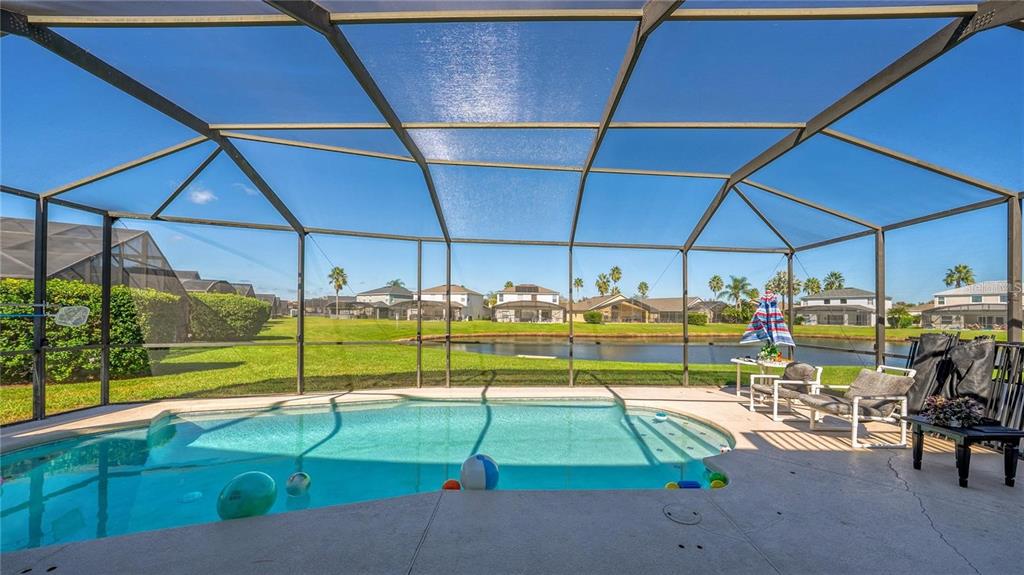 A screened-in swimming pool patio overlooks a pond and residential homes in the background — 1202 CUMBRIAN LAKES COURT, KISSIMMEE, FL