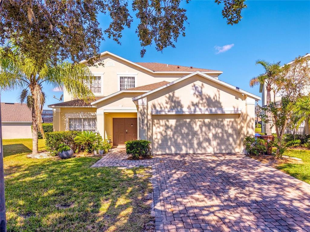 A two-story suburban house features a paved driveway, a double garage, and a front entrance — 1202 CUMBRIAN LAKES COURT, KISSIMMEE, FL