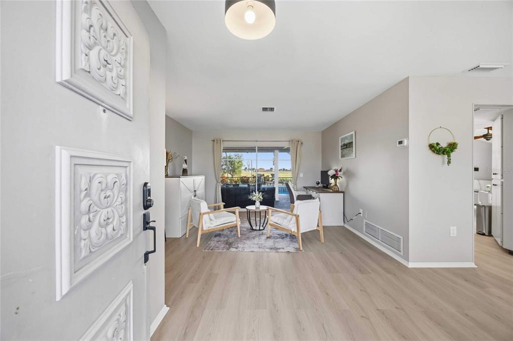 A living area with light wood flooring, two white chairs, and a view of a pool — 36 BUNKER CIRCLE, ROTONDA WEST, FL