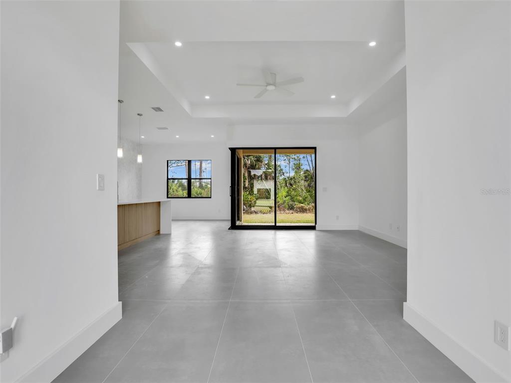 An open-concept living area features large gray floor tiles, a tray ceiling, and sliding glass doors — 11225 CARNEGIE AVENUE, ENGLEWOOD, FL