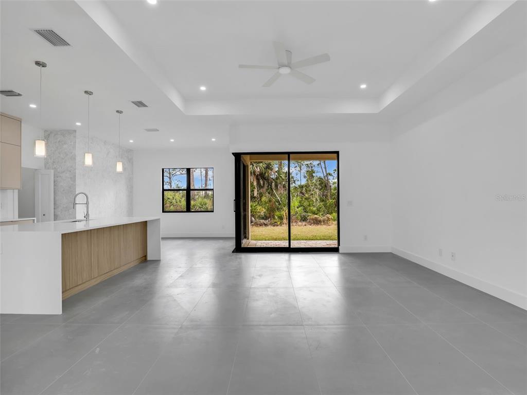 A modern open-concept kitchen and living area features a large island, tile floors, and sliding doors — 11225 CARNEGIE AVENUE, ENGLEWOOD, FL