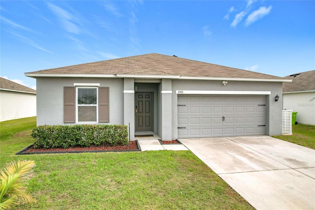 A single-story house with a gray stucco exterior, brown roof, and an attached two-car garage — 440 BURNHAM CIRCLE, AUBURNDALE, FL