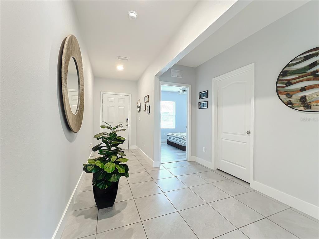A tiled hallway features a large round mirror, a potted plant, and a doorway entrance — 440 BURNHAM CIRCLE, AUBURNDALE, FL