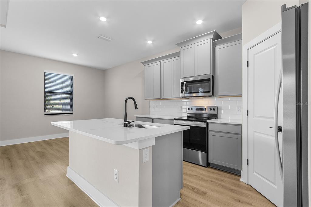 A kitchen features a white island, grey cabinets, stainless steel appliances, and light wood flooring — 13515 WALDEN SHEFFIELD ROAD, DOVER, FL