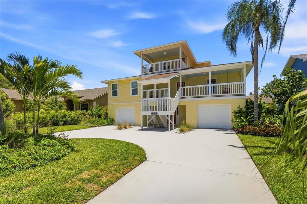 A yellow two-story house with a raised porch, white railings, and a concrete driveway — 433 MONTE CRISTO BOULEVARD, TIERRA VERDE, FL