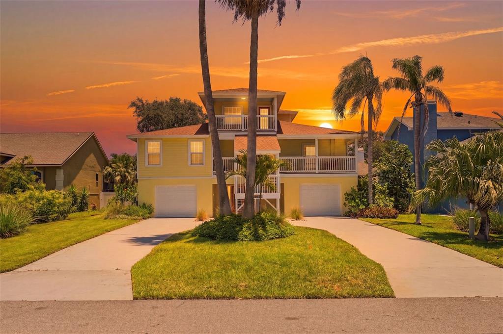 A yellow two-story house with two garage doors and a balcony at sunset — 433 MONTE CRISTO BOULEVARD, TIERRA VERDE, FL