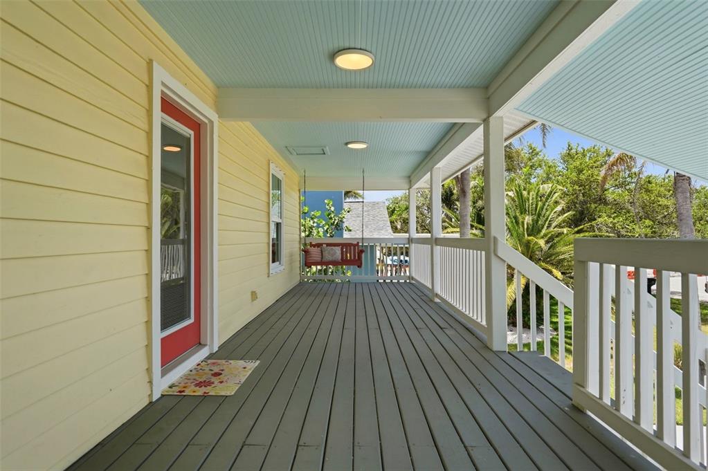 A covered wooden porch features a red door, a porch swing, and light blue ceiling — 433 MONTE CRISTO BOULEVARD, TIERRA VERDE, FL