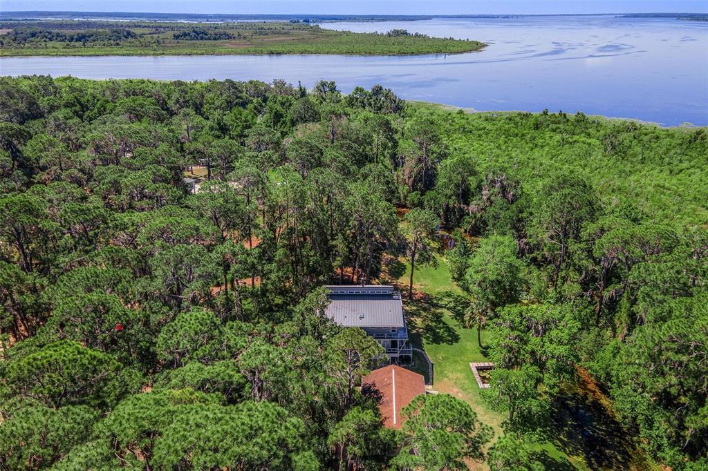 An aerial view shows a house nestled in a dense forest near a large lake — 7373 CIRCLE DRIVE, LADY LAKE, FL