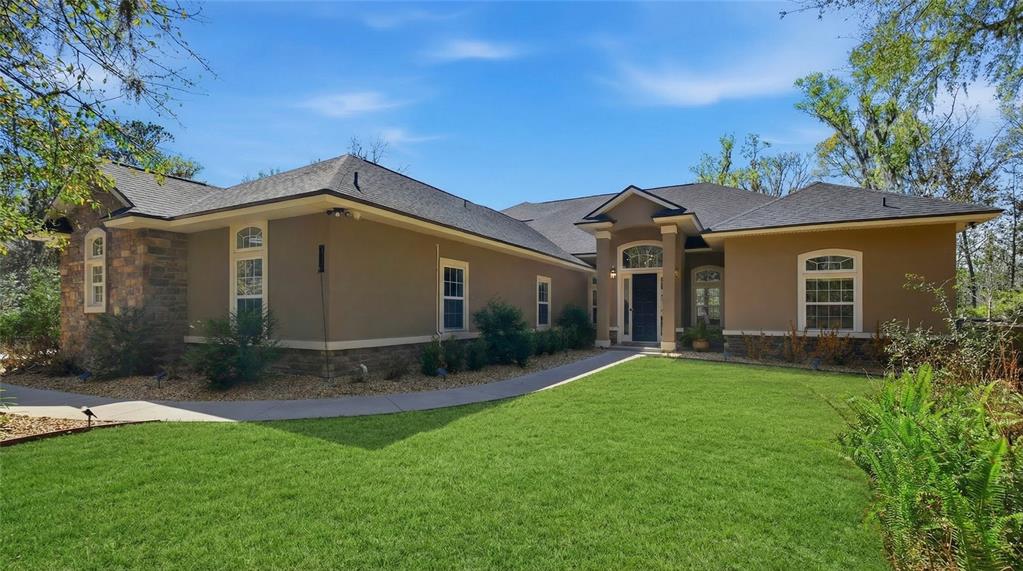 A single-story house with a tan stucco exterior, stone accents, and a dark shingled roof — 6595 COLLIER ROAD, ST AUGUSTINE, FL
