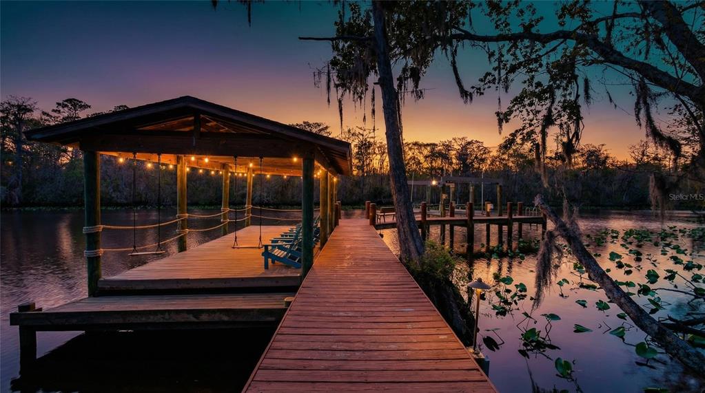 A wooden dock with a covered seating area extends over a lake at sunset — 6595 COLLIER ROAD, ST AUGUSTINE, FL
