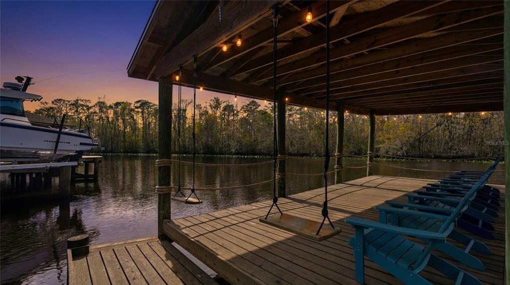 A wooden boat dock features two hanging swings, blue chairs, and string lights at sunset — 6595 COLLIER ROAD, ST AUGUSTINE, FL