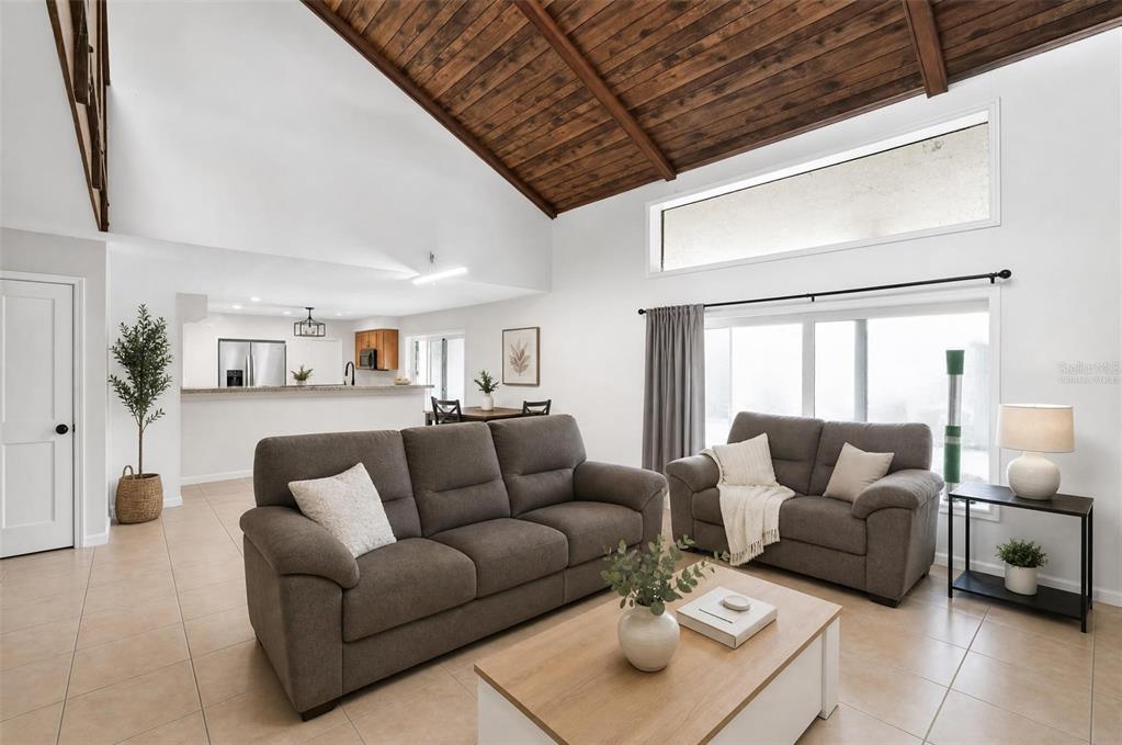 A living room with a vaulted wood-paneled ceiling, tile flooring, and an open kitchen view — 310 HIDDEN LAKE DRIVE, BRANDON, FL