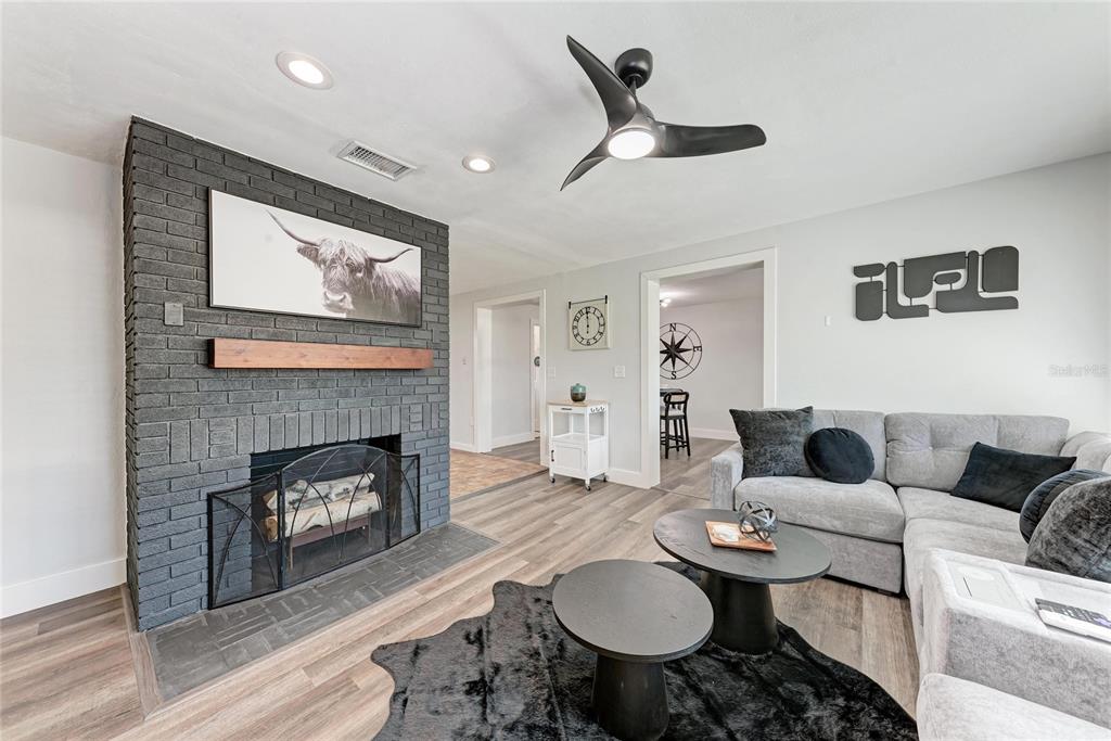 A living room features a gray brick fireplace, wood-look flooring, and a modern ceiling fan — 339 SUWANEE AVENUE, SARASOTA, FL