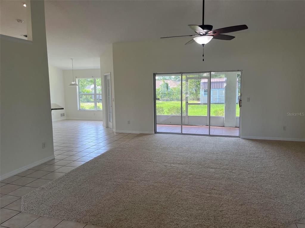 A spacious living area with beige carpeting, tile flooring, and an open kitchen in the background — 4949 SW 109TH LOOP, OCALA, FL
