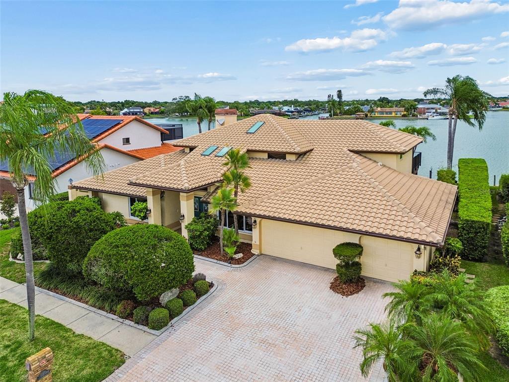 An aerial view shows a tan house with a tiled roof, garage, and waterfront backyard — 9815 BAY ISLAND DRIVE, TAMPA, FL