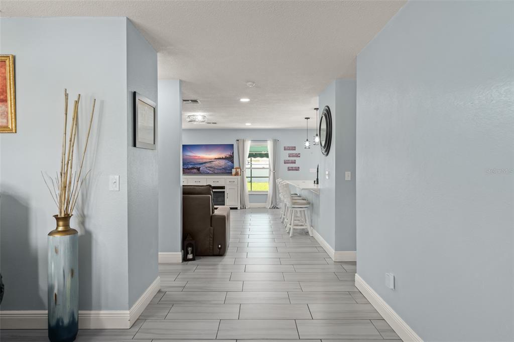 A hallway with light gray tile flooring leads into an open living area and kitchen — 15272 SUGARGROVE WAY, ORLANDO, FL
