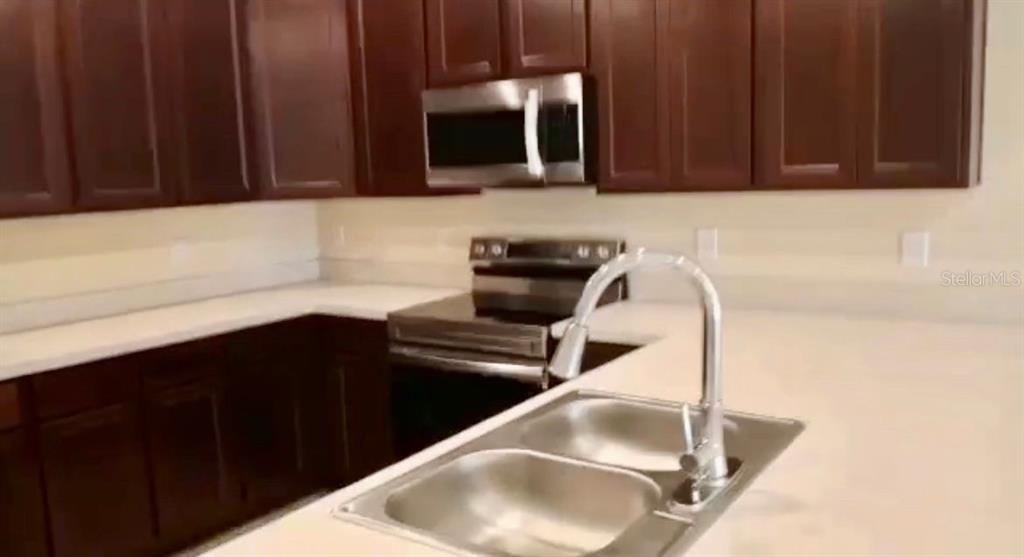 A kitchen features dark wood cabinets, stainless steel appliances, and a white countertop — 4812 CORAL CASTLE DRIVE, KISSIMMEE, FL