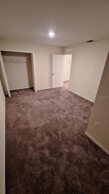 An empty bedroom with brown carpet, a walk-in closet, and an open doorway — 4812 CORAL CASTLE DRIVE, KISSIMMEE, FL
