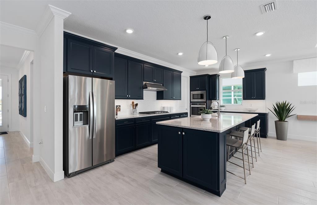 A modern kitchen features dark blue cabinetry, stainless steel appliances, and a large central island — 1313 ZESTY CITRUS LANE, MINNEOLA, FL