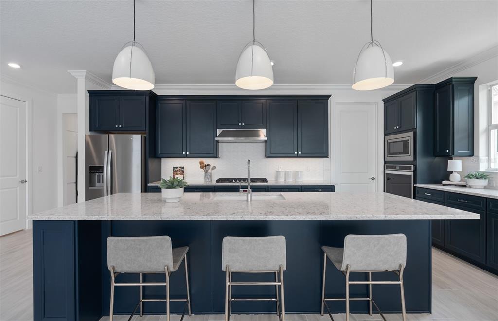 A modern kitchen features dark blue cabinets, a large quartz island, and three white pendant lights — 1313 ZESTY CITRUS LANE, MINNEOLA, FL