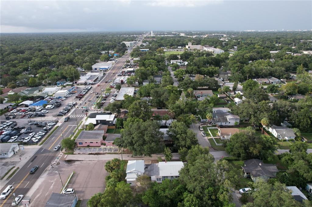 An aerial view shows a street with parked cars, surrounding houses, and dense green trees — 6506 N WELLINGTON AVENUE, TAMPA, FL
