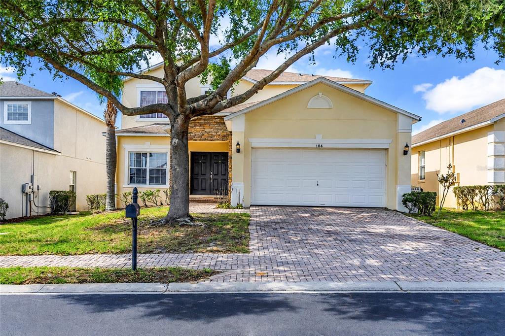 A two-story yellow house with a stone facade, a white garage door, and a brick driveway — 164 LANCASTER DRIVE, DAVENPORT, FL