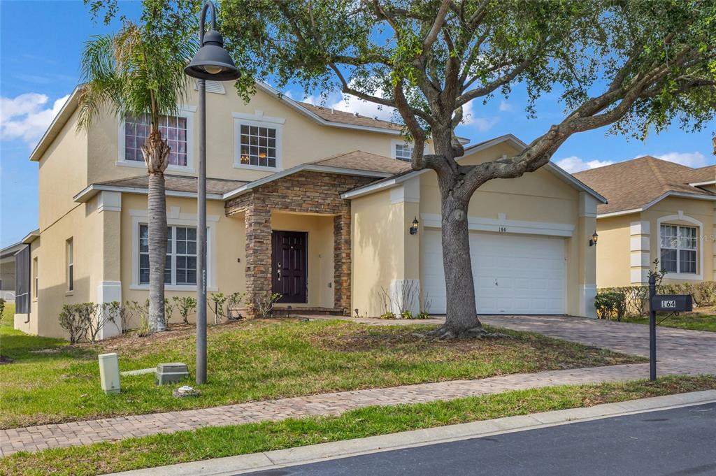 A two-story suburban house with a stone-accented entryway, a two-car garage, and a large tree — 164 LANCASTER DRIVE, DAVENPORT, FL
