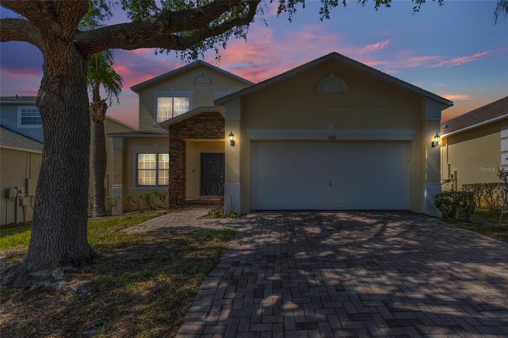 A two-story house with a paved driveway, stone accents, and a two-car garage at dusk — 164 LANCASTER DRIVE, DAVENPORT, FL